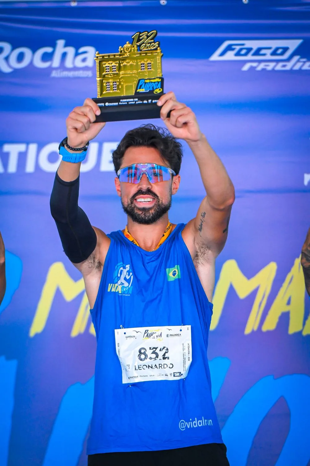 Atleta levanta o troféu diante do painel da prova
